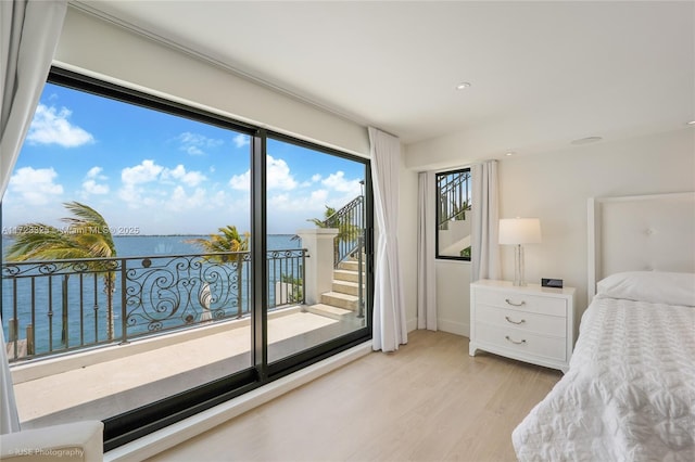 bedroom with a water view, light wood-type flooring, and access to outside