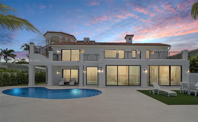 back house at dusk featuring a balcony and a patio area