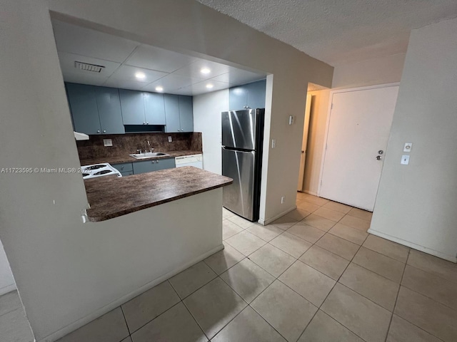 kitchen featuring kitchen peninsula, stainless steel fridge, backsplash, sink, and blue cabinetry