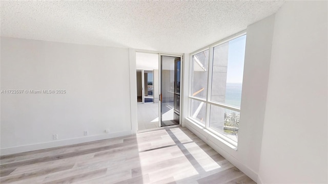 empty room with a textured ceiling, expansive windows, a water view, and light hardwood / wood-style flooring