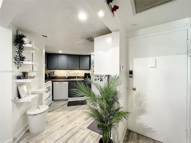 kitchen with white dishwasher, wall oven, light wood-type flooring, and a textured ceiling