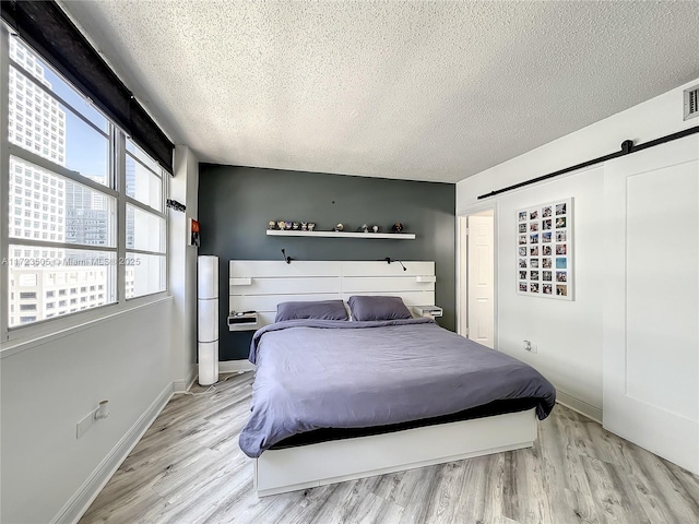 bedroom with a barn door, a textured ceiling, and light hardwood / wood-style flooring