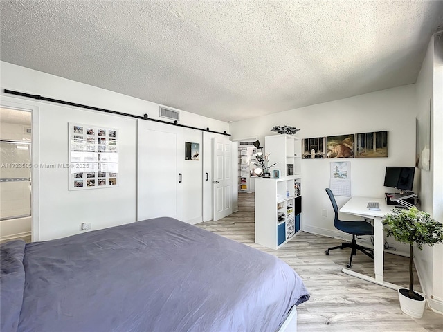 bedroom with light wood-type flooring, a textured ceiling, a barn door, and ensuite bath