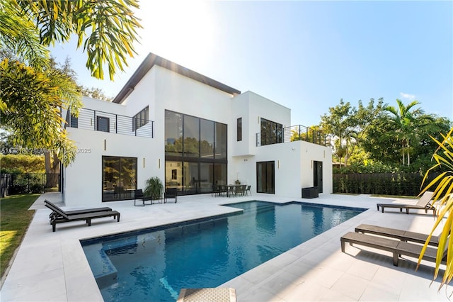 rear view of house featuring a patio area, a balcony, and a fenced in pool