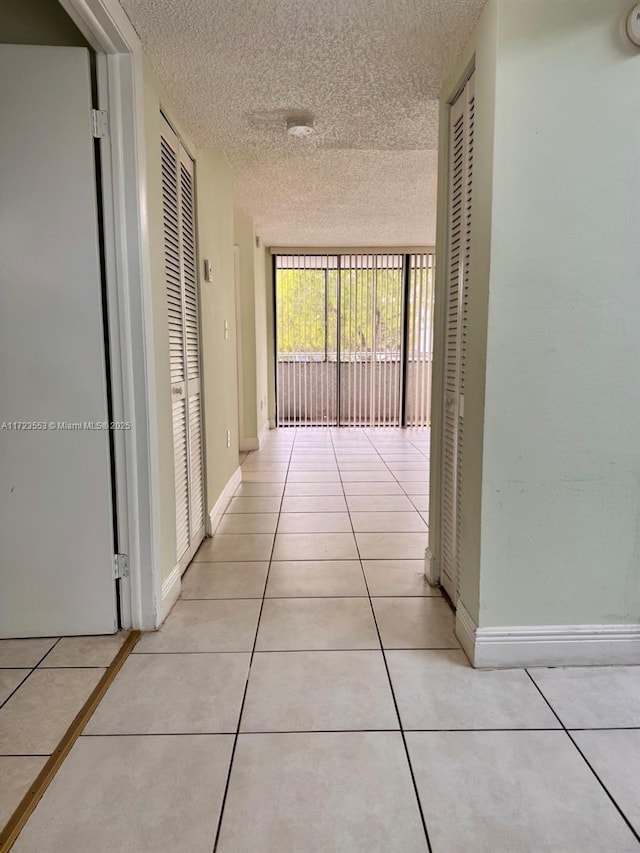 corridor with expansive windows, light tile patterned floors, and a textured ceiling