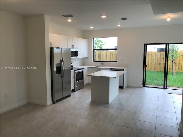 kitchen featuring white cabinets, sink, light tile patterned floors, appliances with stainless steel finishes, and a kitchen island