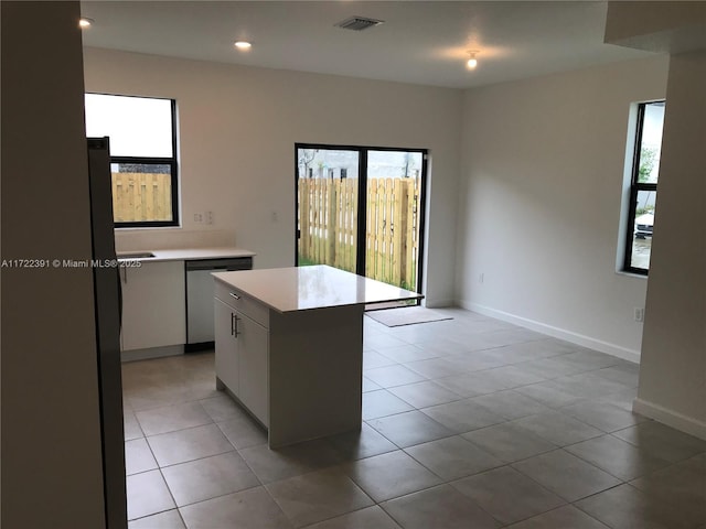 kitchen with white cabinets, light tile patterned flooring, a kitchen island, and stainless steel dishwasher