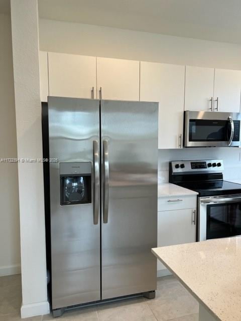 kitchen featuring light stone countertops, light tile patterned floors, stainless steel appliances, and white cabinetry