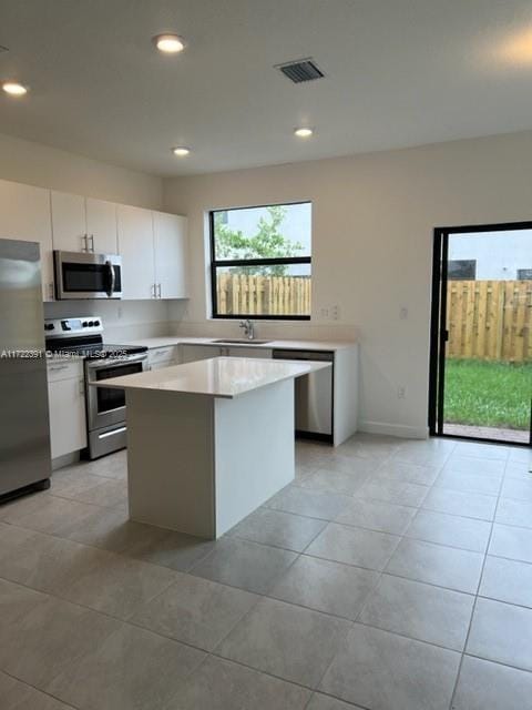 kitchen with a wealth of natural light, white cabinetry, a center island, sink, and appliances with stainless steel finishes