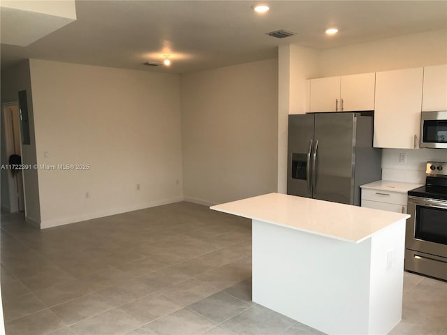 kitchen with white cabinets, a kitchen island, light tile patterned floors, and appliances with stainless steel finishes