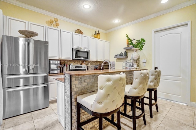 kitchen featuring stainless steel appliances, crown molding, a center island with sink, white cabinetry, and a breakfast bar area