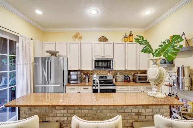 kitchen with white cabinets, a kitchen breakfast bar, ornamental molding, and appliances with stainless steel finishes