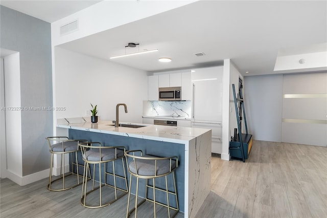 kitchen featuring a breakfast bar area, kitchen peninsula, white cabinetry, and sink