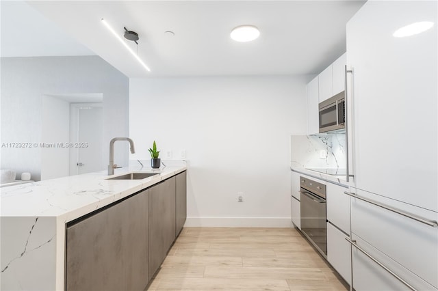 kitchen with light stone countertops, sink, light hardwood / wood-style flooring, white cabinets, and oven