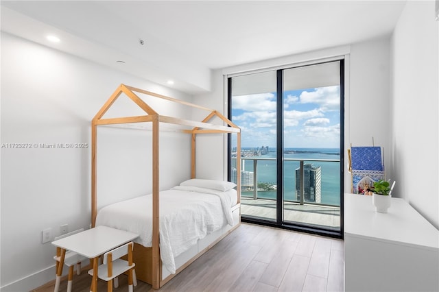 bedroom featuring access to exterior, floor to ceiling windows, a water view, and light wood-type flooring