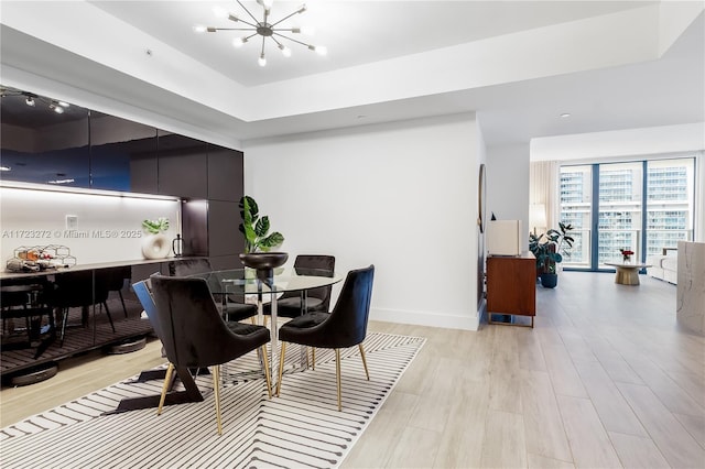 dining room featuring a raised ceiling, a chandelier, and light hardwood / wood-style floors