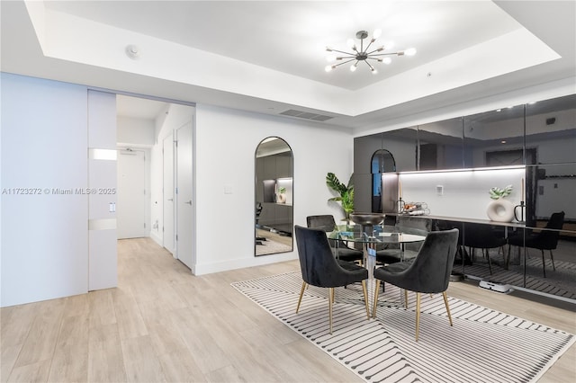 dining space featuring a raised ceiling, light wood-type flooring, and a chandelier