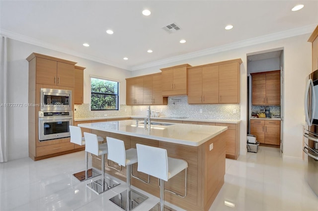 kitchen featuring sink, an island with sink, appliances with stainless steel finishes, light tile patterned flooring, and a breakfast bar area