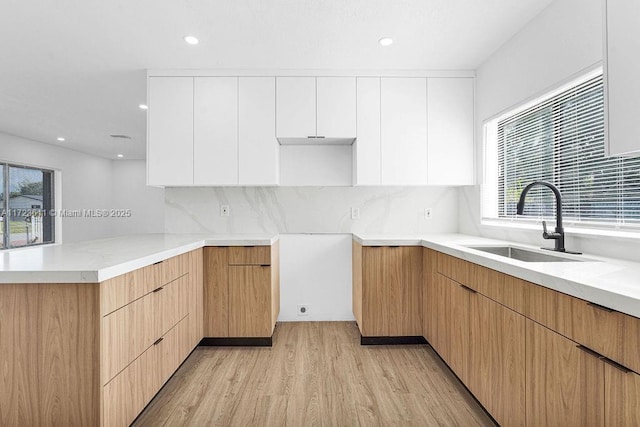 kitchen with backsplash, sink, light hardwood / wood-style flooring, white cabinetry, and kitchen peninsula