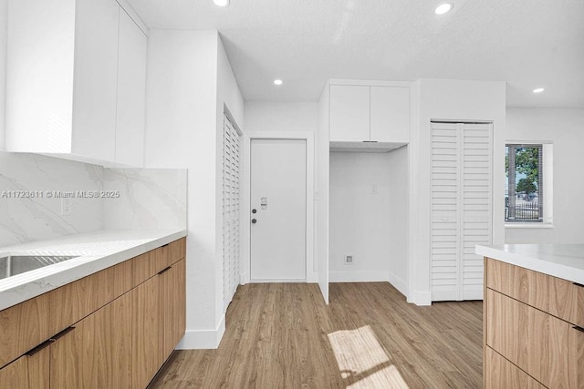 kitchen with a textured ceiling, light hardwood / wood-style floors, white cabinetry, and tasteful backsplash