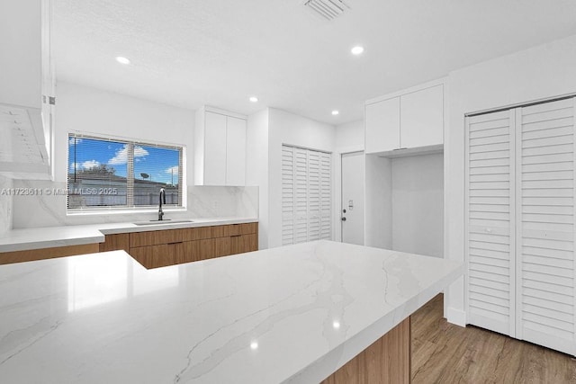 kitchen with light stone countertops, tasteful backsplash, sink, light hardwood / wood-style floors, and white cabinetry