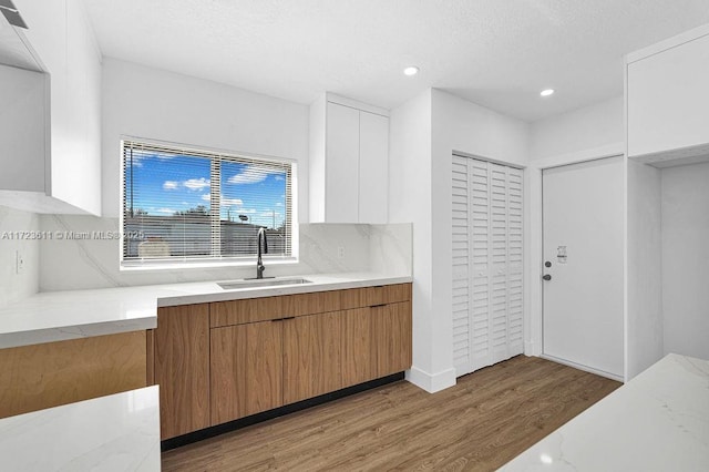 kitchen featuring white cabinets, sink, decorative backsplash, light hardwood / wood-style floors, and light stone counters