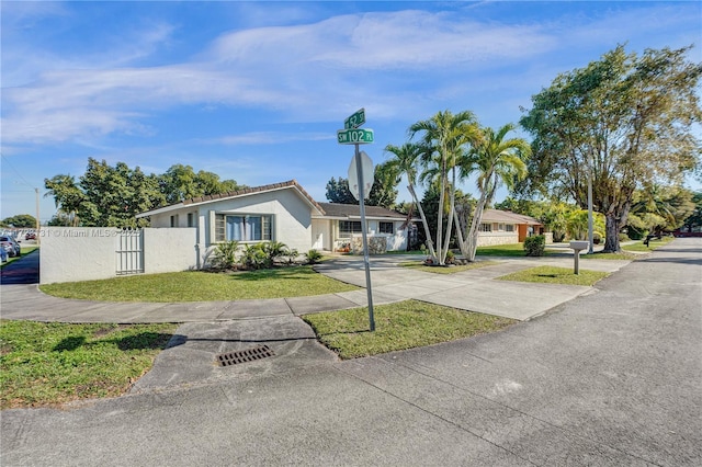 ranch-style house with driveway, a front yard, a tile roof, stucco siding, and fence