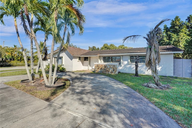ranch-style house with a front yard, a tiled roof, concrete driveway, and stucco siding