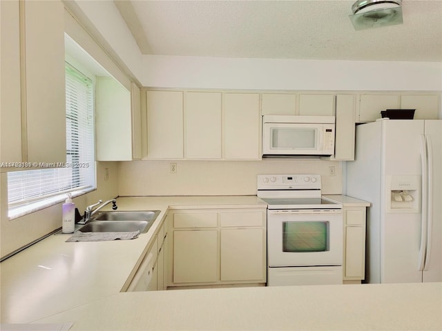 kitchen with light countertops, cream cabinets, white appliances, a textured ceiling, and a sink