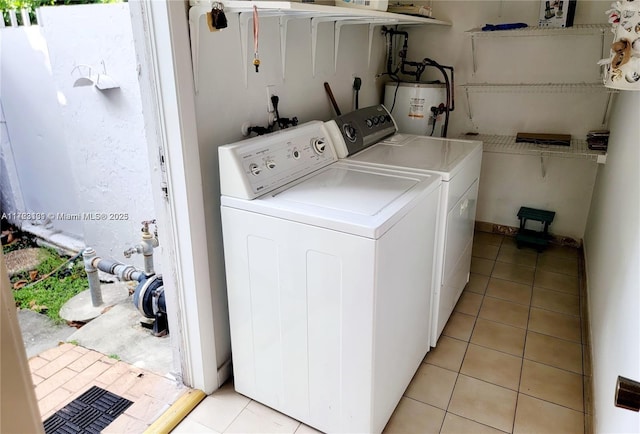 laundry room featuring water heater, light tile patterned flooring, washing machine and clothes dryer, and laundry area