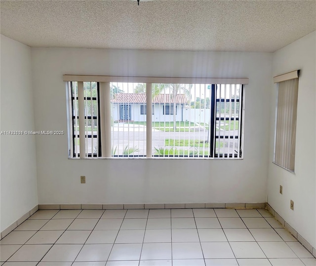 tiled empty room with baseboards and a textured ceiling