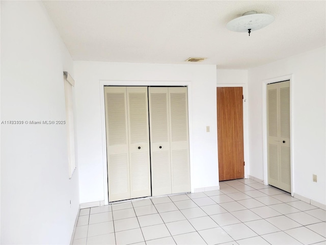 unfurnished bedroom featuring a closet, baseboards, visible vents, and light tile patterned floors