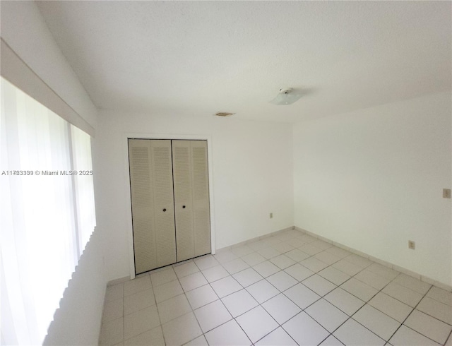 unfurnished bedroom with light tile patterned floors, visible vents, a closet, and baseboards