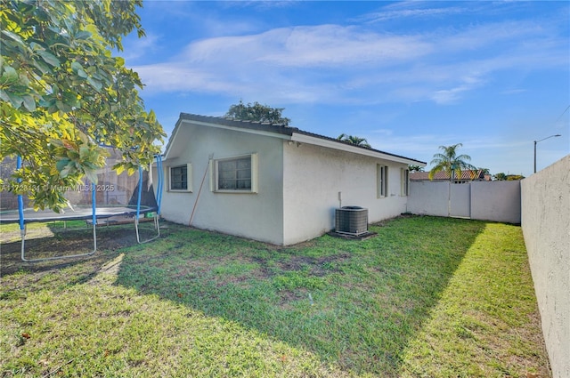 exterior space with stucco siding, a fenced backyard, a trampoline, central AC, and a lawn