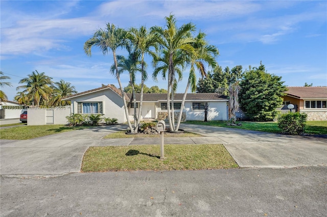 ranch-style house with concrete driveway, fence, a front lawn, and stucco siding