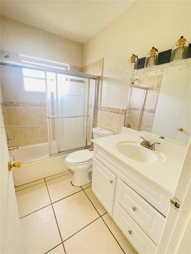 full bathroom featuring tile patterned floors, bath / shower combo with glass door, vanity, tile walls, and toilet