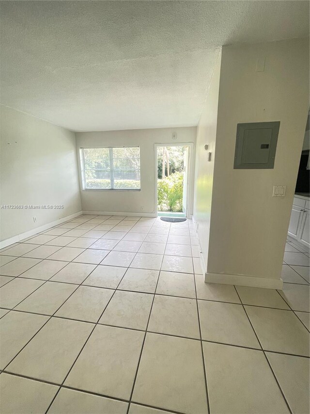 tiled spare room featuring a textured ceiling, electric panel, and a healthy amount of sunlight