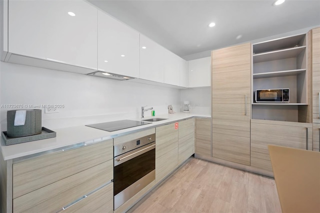 kitchen featuring oven, sink, light wood-type flooring, black electric cooktop, and white cabinetry