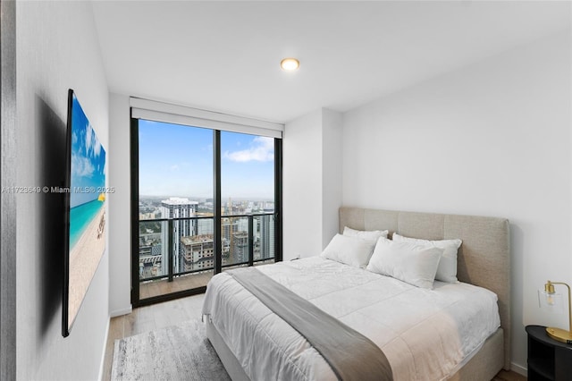 bedroom featuring access to exterior, light wood-type flooring, and a wall of windows