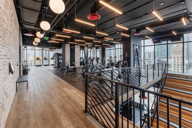 exercise room with a wall of windows, brick wall, and hardwood / wood-style flooring