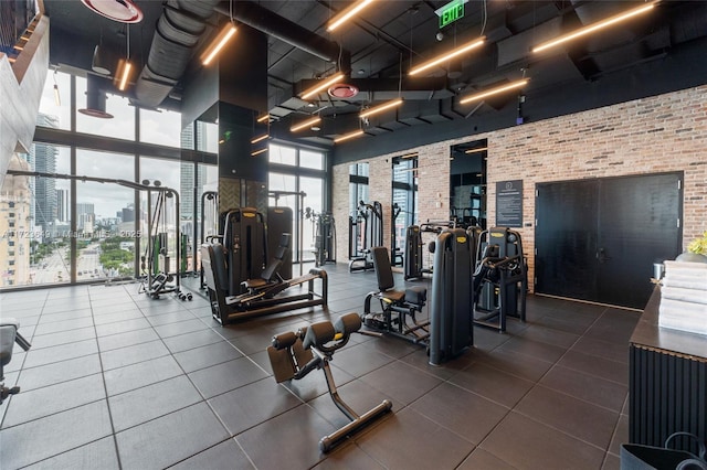 exercise room featuring floor to ceiling windows, brick wall, and a high ceiling