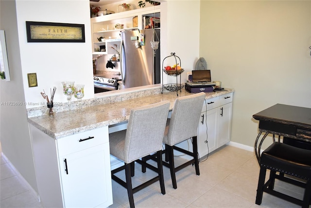 kitchen featuring white cabinetry, light stone countertops, a breakfast bar, light tile patterned floors, and appliances with stainless steel finishes