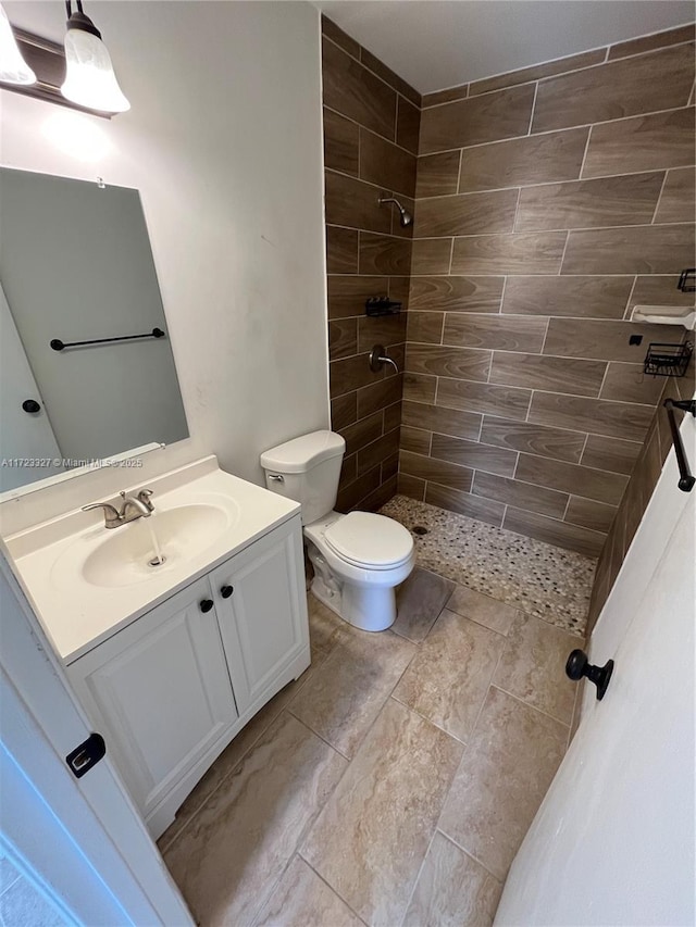 bathroom with a tile shower, vanity, and toilet