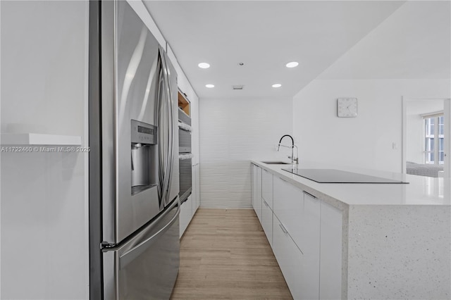 kitchen featuring sink, stainless steel appliances, light hardwood / wood-style floors, white cabinets, and tile walls