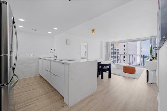 kitchen featuring stainless steel refrigerator, white cabinetry, sink, expansive windows, and light wood-type flooring