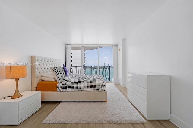 bedroom with access to exterior, a water view, light hardwood / wood-style flooring, and a wall of windows