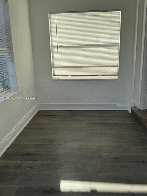 spare room with dark wood finished floors, a healthy amount of sunlight, and baseboards