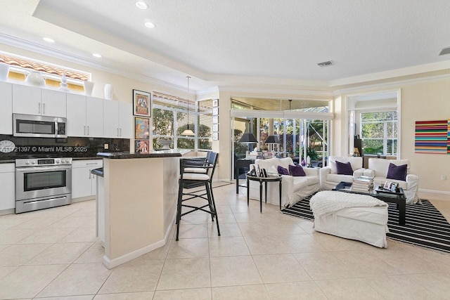 kitchen with decorative backsplash, appliances with stainless steel finishes, a kitchen breakfast bar, light tile patterned floors, and white cabinets