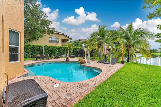 view of swimming pool featuring a yard, a water view, and a patio