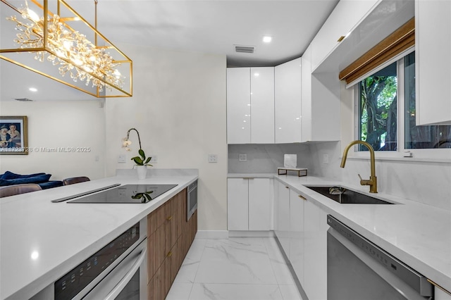 kitchen featuring stainless steel appliances, sink, pendant lighting, white cabinets, and a chandelier